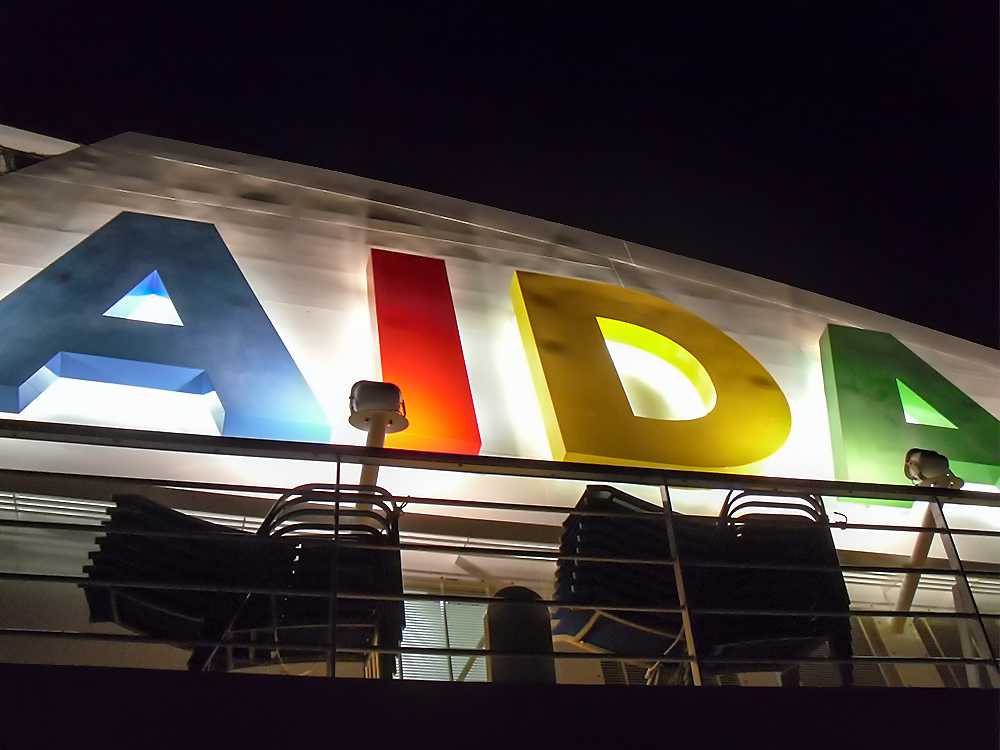 AIDAblu (AIDA Cruises) - beleuchtetes AIDA-Logo am Schornstein bei Nacht
